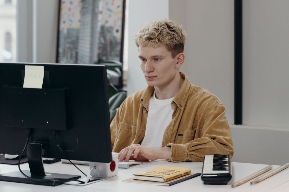 A young man working at a computer with a notebook beside him
