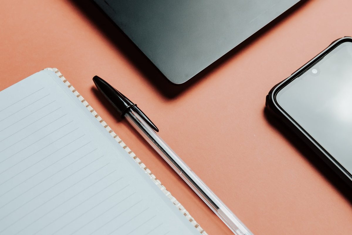 A notebook, pen, phone and laptop laid out on a desk