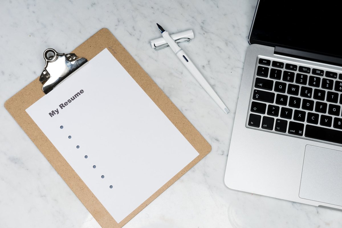 A printed resume checklist on a clipboard beside a laptop and fountain pen