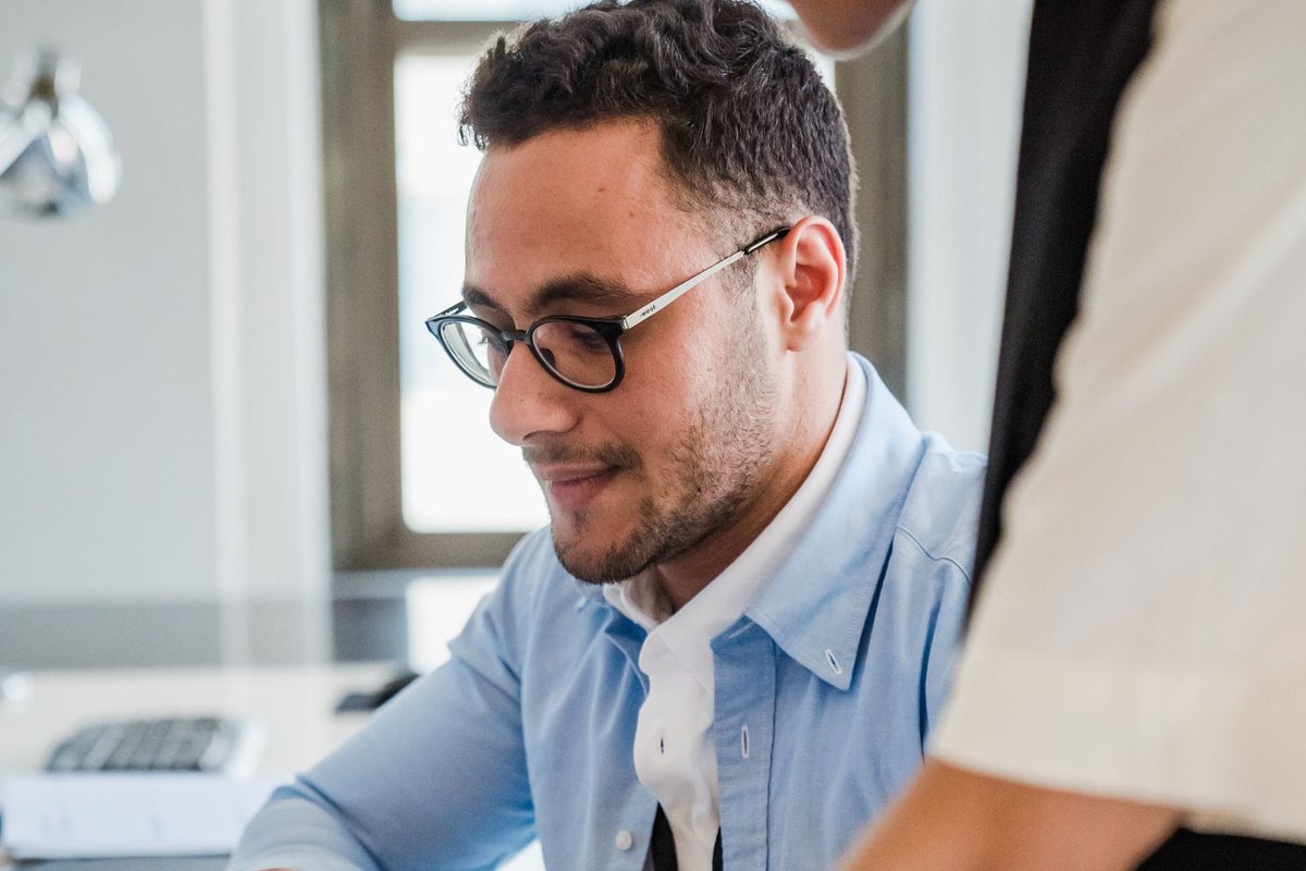 A man smiling while working on a laptop in an office